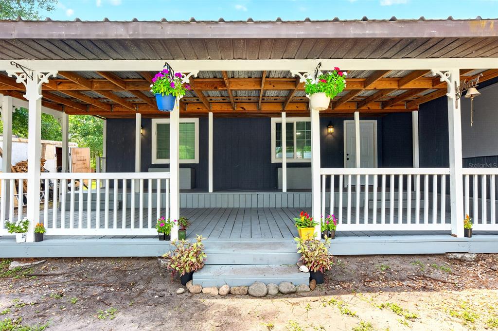 A covered wooden porch with white railings and hanging flower baskets in front of a house — 4585 VANCOUVER AVENUE, COCOA, FL