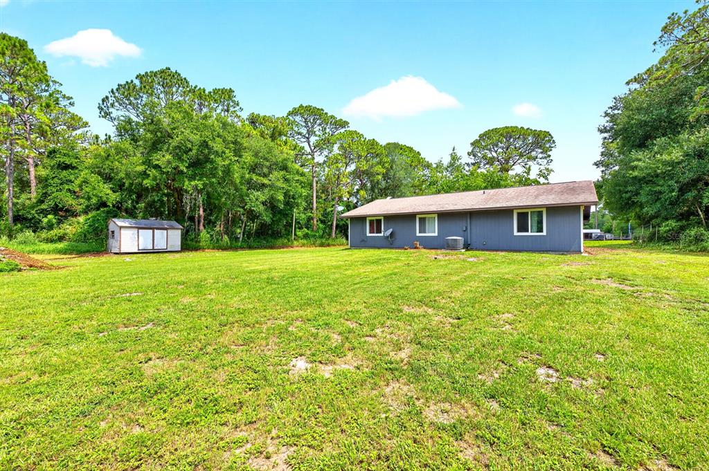 A backyard view shows a gray house, a small shed, and trees under a blue sky — 4585 VANCOUVER AVENUE, COCOA, FL