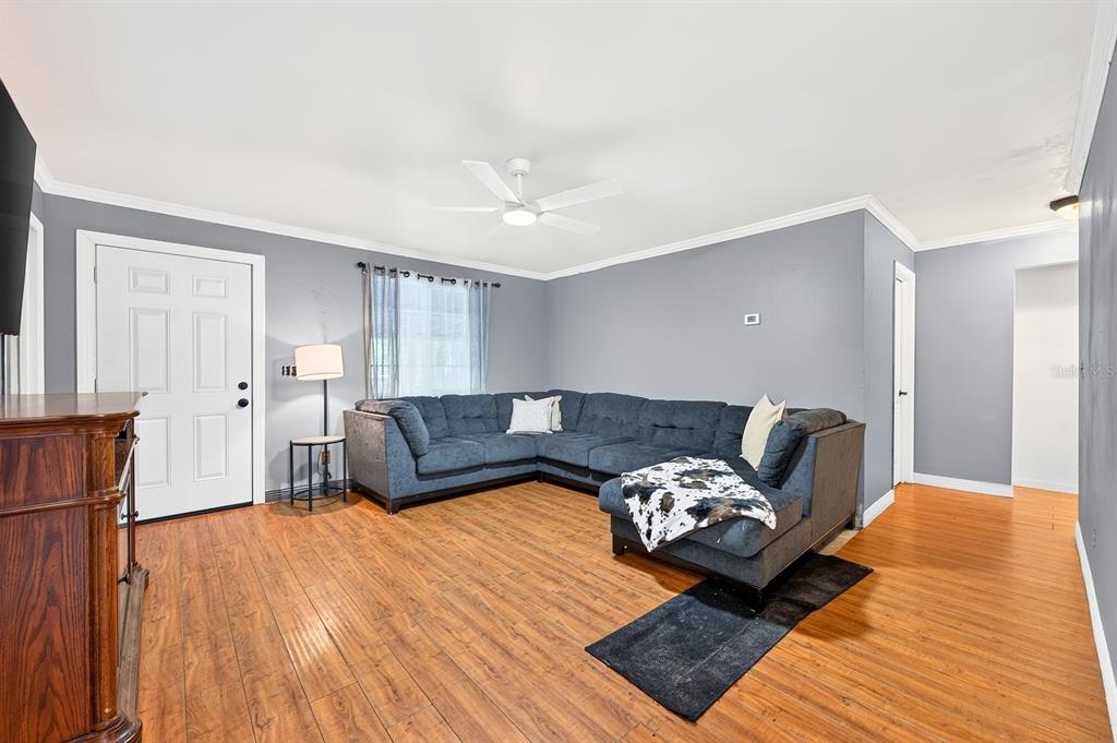 A living room features gray walls, wood-look flooring, a large blue sectional, and a ceiling fan — 4585 VANCOUVER AVENUE, COCOA, FL