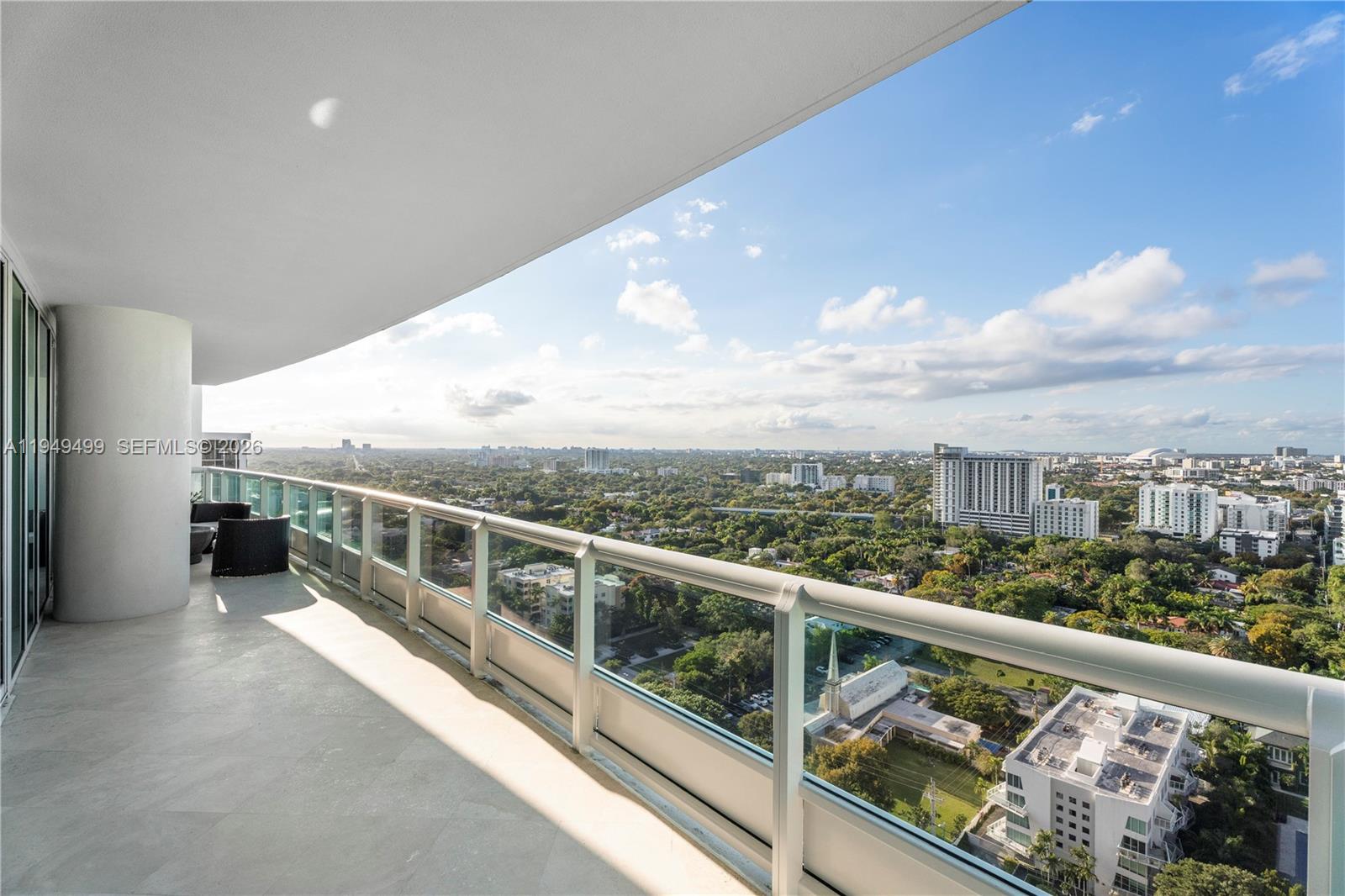 A high-rise balcony features a glass railing overlooking a sprawling city and lush landscape — 1643 Brickell Ave # 2506, Miami FL 33129, MIAMI, FL