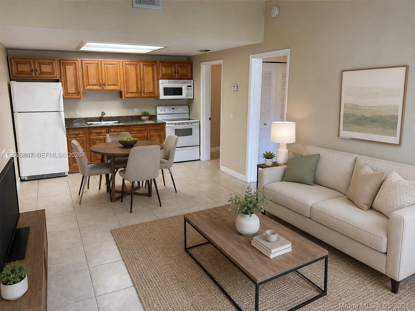 An open-concept living and dining area features tile flooring, wood cabinets, and a neutral sofa — TAMARAC, FL
