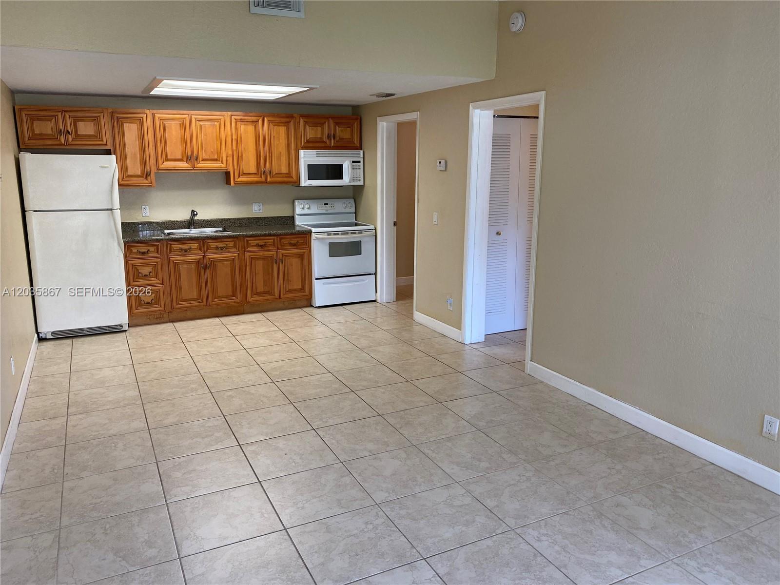 A kitchen with wood cabinets, white appliances, and tiled flooring opens into an adjacent room — TAMARAC, FL
