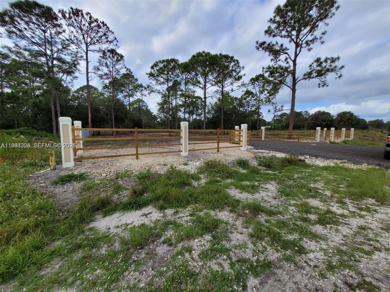 A gravel driveway leads to a fenced vacant lot with tall pine trees — 610 S Quebrada St, Clewiston FL 33440, CLEWISTON, FL