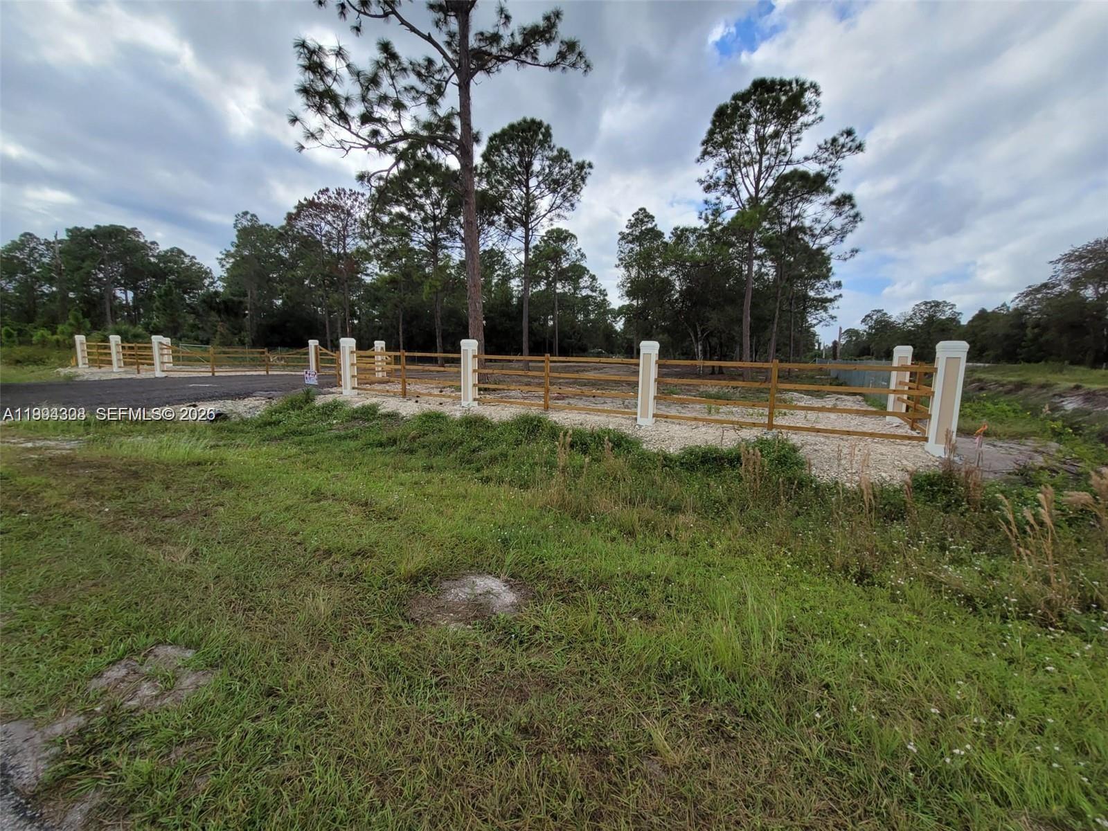 A wooden fence with white pillars borders a gravel area in front of trees — 610 S Quebrada St, Clewiston FL 33440, CLEWISTON, FL