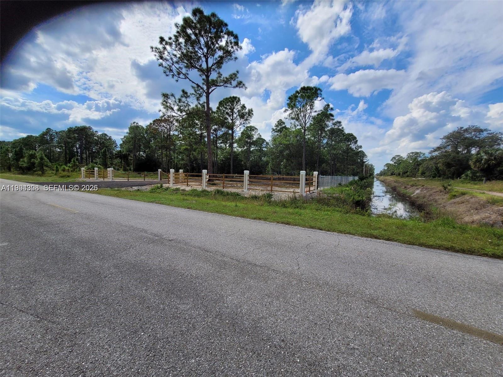 A paved road runs alongside a fenced lot with trees and a drainage canal — 610 S Quebrada St, Clewiston FL 33440, CLEWISTON, FL