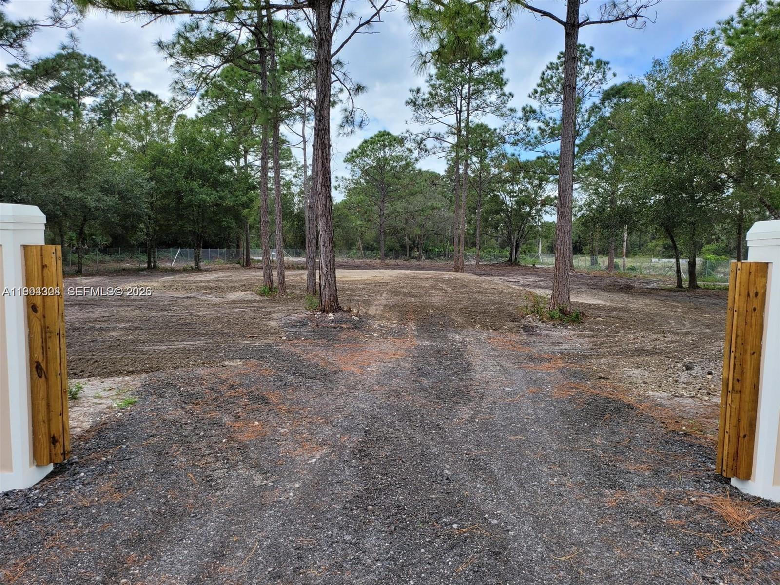 A gravel driveway leads to a cleared, wooded lot framed by two white gate pillars — 610 S Quebrada St, Clewiston FL 33440, CLEWISTON, FL