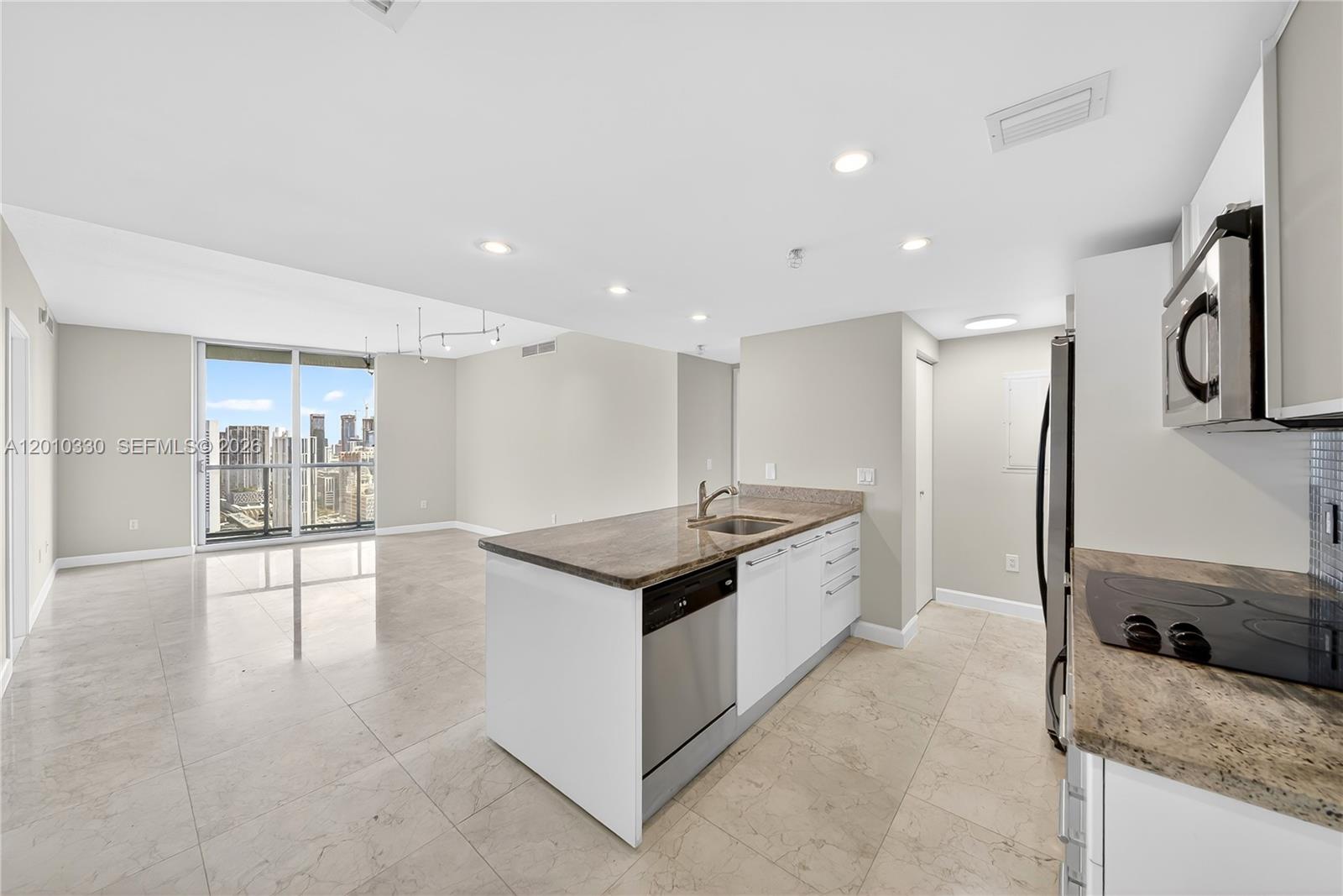 A modern kitchen with a granite-topped island overlooks an open living area with city views — 185 SW 7th St # 4209, Miami FL 33130, MIAMI, FL