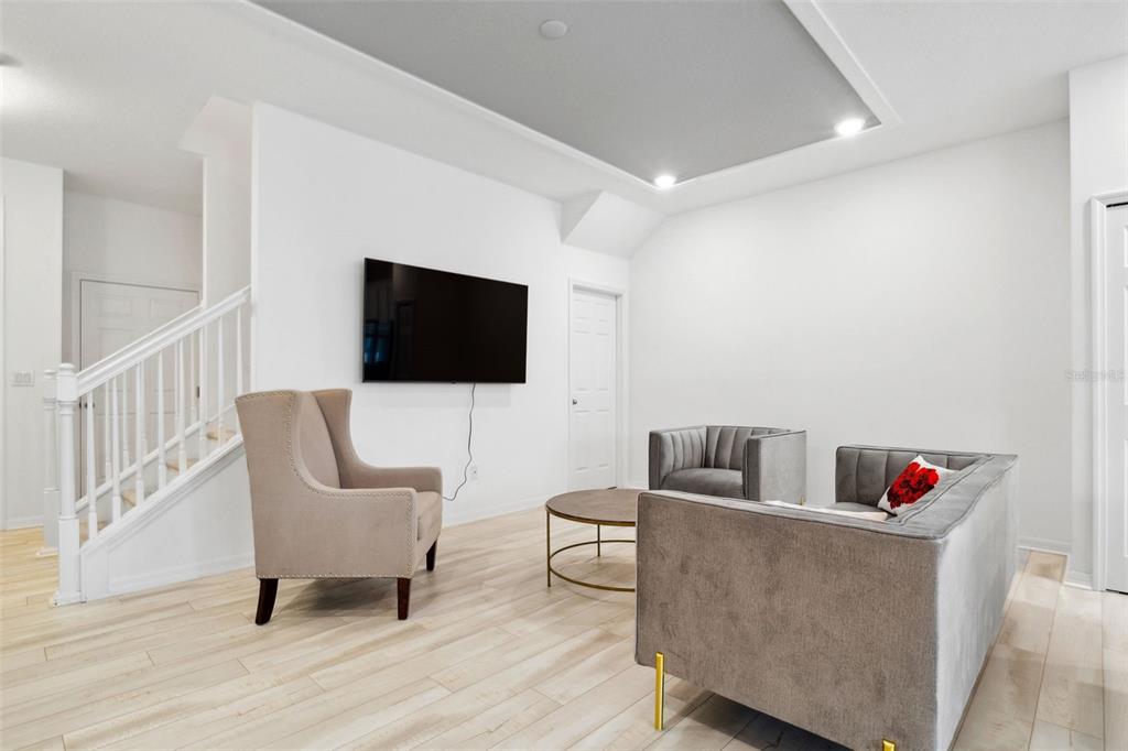 A living room features light wood flooring, a mounted television, and grey upholstered seating — 5732 SKYTOP DRIVE, LITHIA, FL