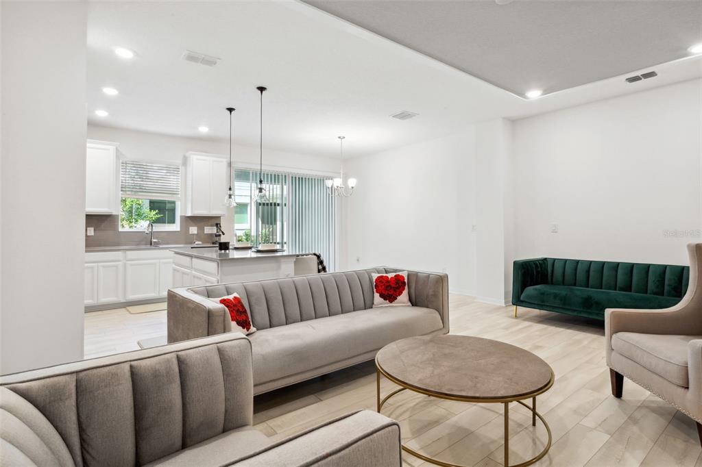 An open-concept living room features light wood floors, gray sofas, and a modern kitchen — 5732 SKYTOP DRIVE, LITHIA, FL