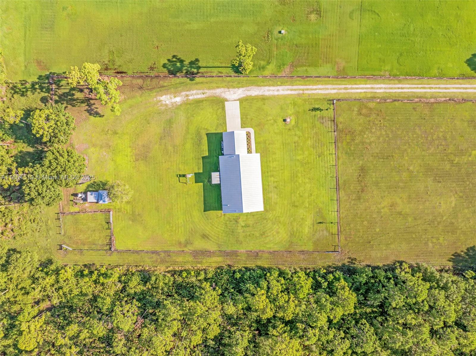 An aerial view shows a house with a metal roof situated on a fenced lot — 99 TRADER RD, La Belle FL 33935, LA BELLE, FL
