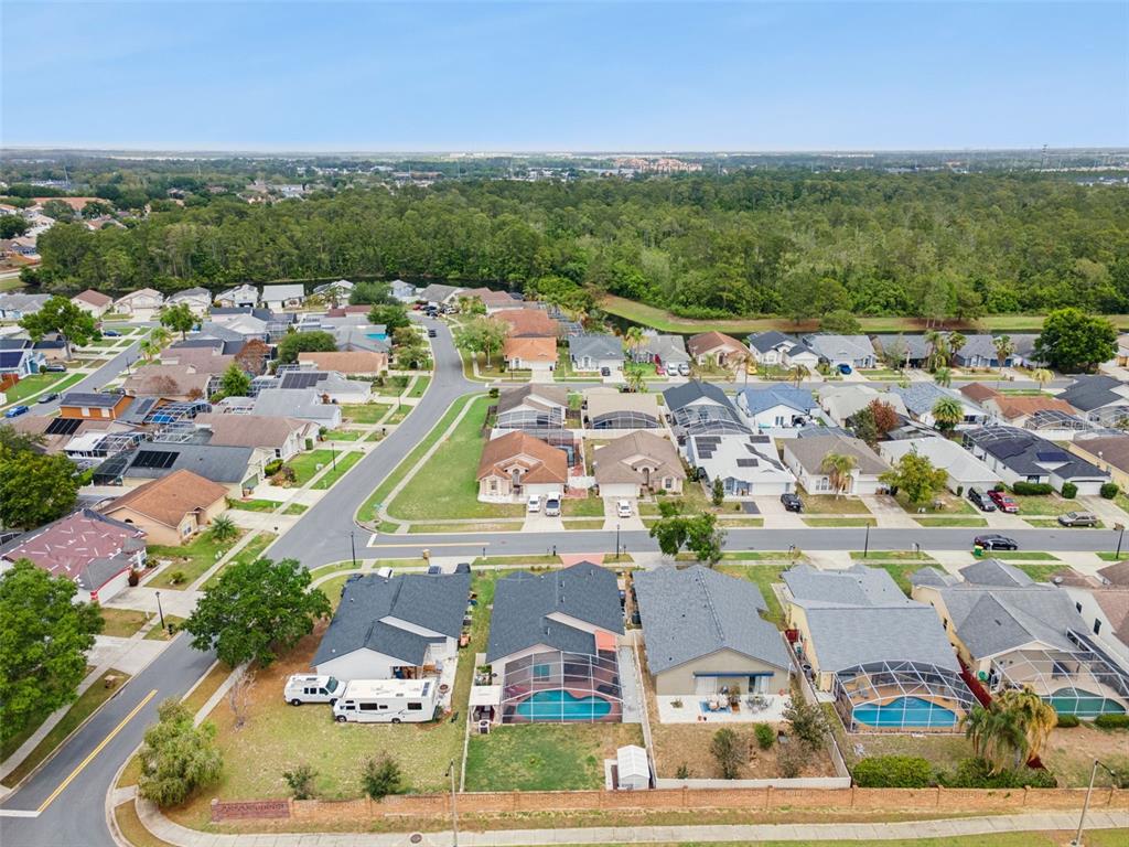 An aerial view shows a suburban neighborhood with houses, swimming pools, and a wooded area — 8602 WELLINGTON LOOP, KISSIMMEE, FL