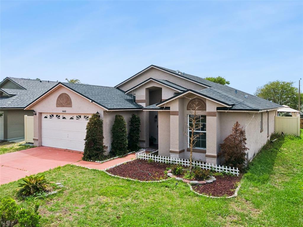 A single-story house with a beige stucco exterior, a two-car garage, and a shingled roof — 8602 WELLINGTON LOOP, KISSIMMEE, FL
