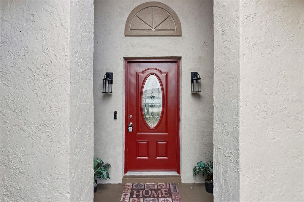 A red front door with a glass oval insert sits between two stucco walls — 8602 WELLINGTON LOOP, KISSIMMEE, FL