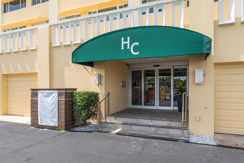 The exterior entrance of a building features a green awning with the letters HC — 100 BLUFF VIEW DRIVE UNIT 506C, BELLEAIR BLUFFS, FL