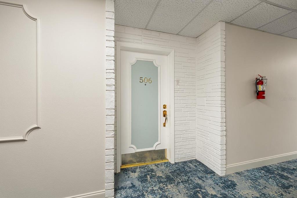 A white door labeled 506 is set within a white brick wall in a hallway — 100 BLUFF VIEW DRIVE UNIT 506C, BELLEAIR BLUFFS, FL