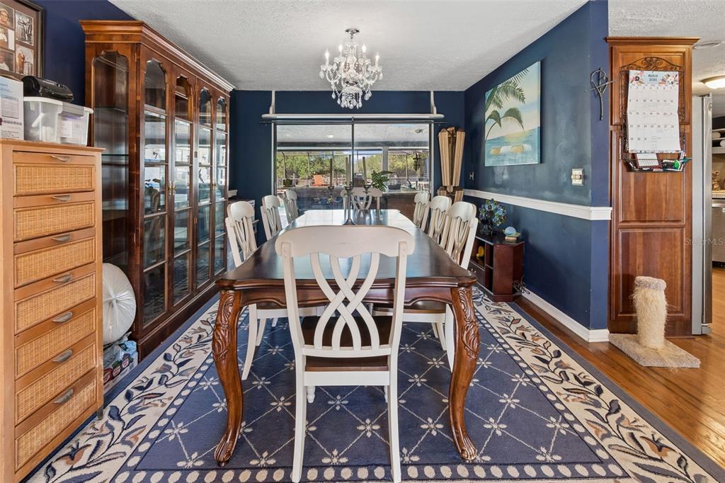 A dining room features a dark wood table, white chairs, a chandelier, and blue walls — 5059 BERNADETTE DRIVE, ZEPHYRHILLS, FL