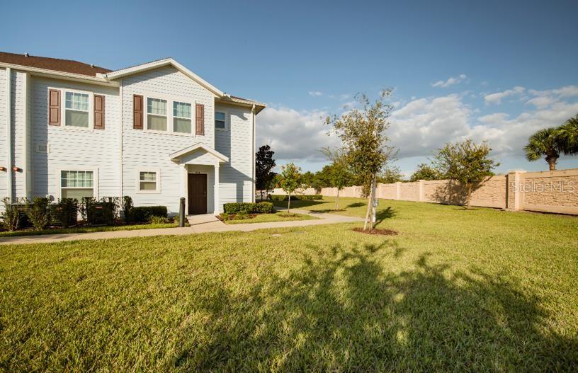A two-story light-colored siding apartment building sits next to a grassy lawn and wall — 3200 CUPID PLACE, KISSIMMEE, FL