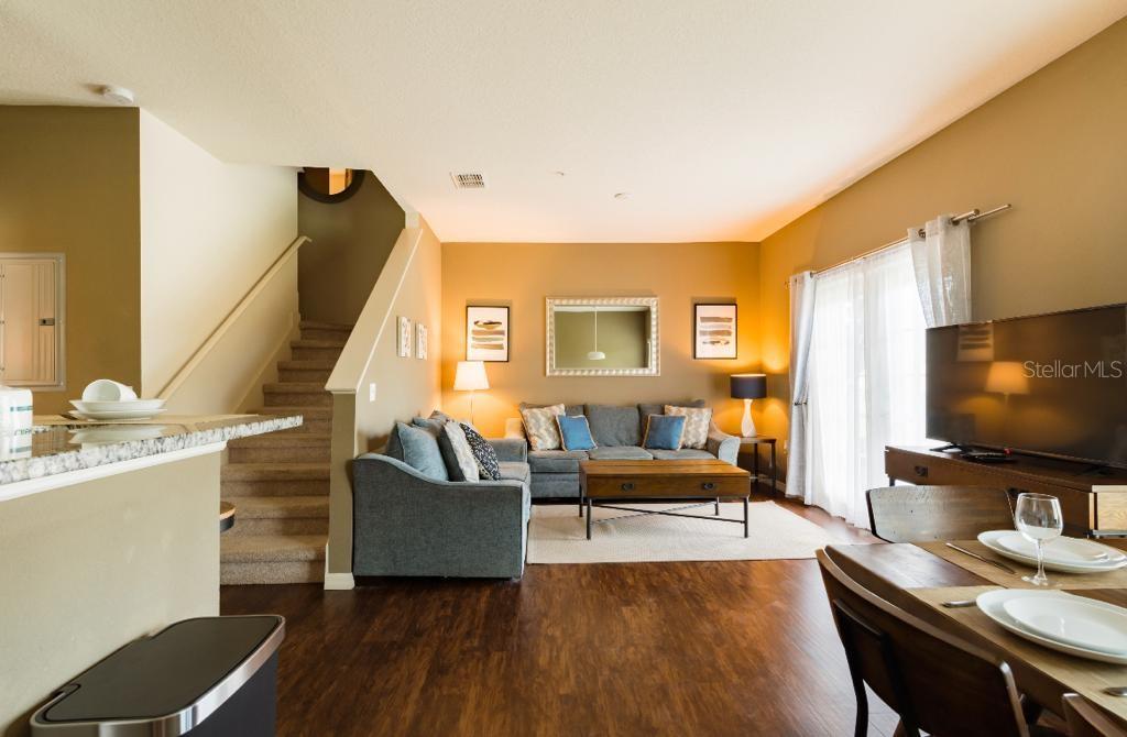 An open-concept living room features a sofa, coffee table, staircase, and dining area with wood flooring — 3200 CUPID PLACE, KISSIMMEE, FL