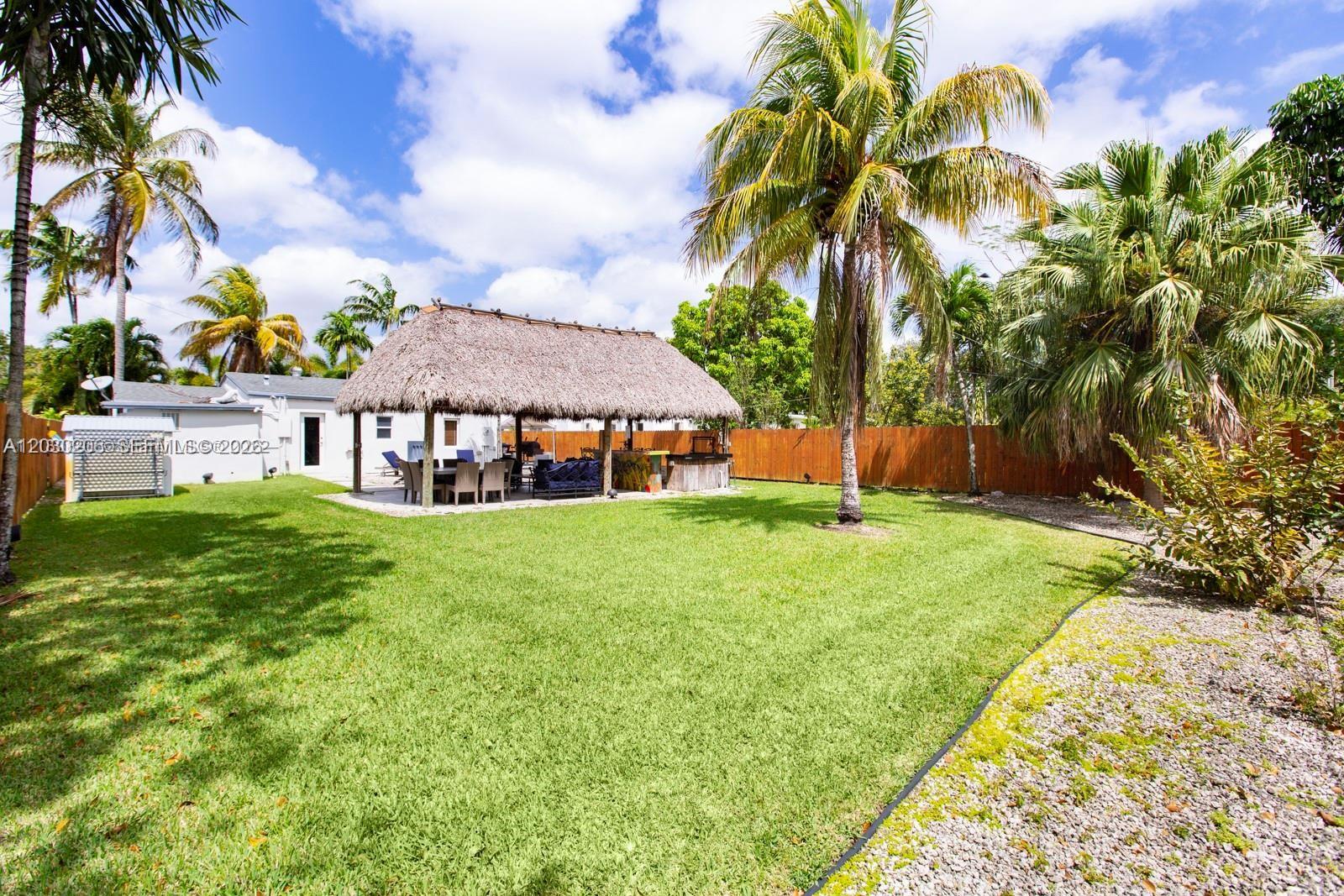 A grassy backyard features a large thatched-roof tiki hut with outdoor seating and a bar — 6530 SW 43rd St, Miami FL 33155, MIAMI, FL
