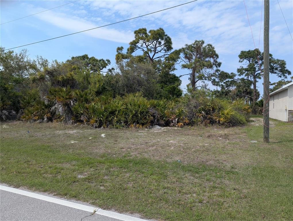 A vacant, grassy lot with dense vegetation and trees sits next to a residential building — 516 SUNSET ROAD N, ROTONDA WEST, FL