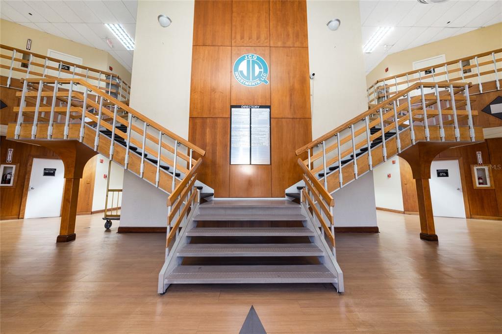 A symmetrical office building lobby features a central staircase leading to a wood-paneled wall — 7200 LAKE ELLENOR DRIVE UNIT 130, ORLANDO, FL