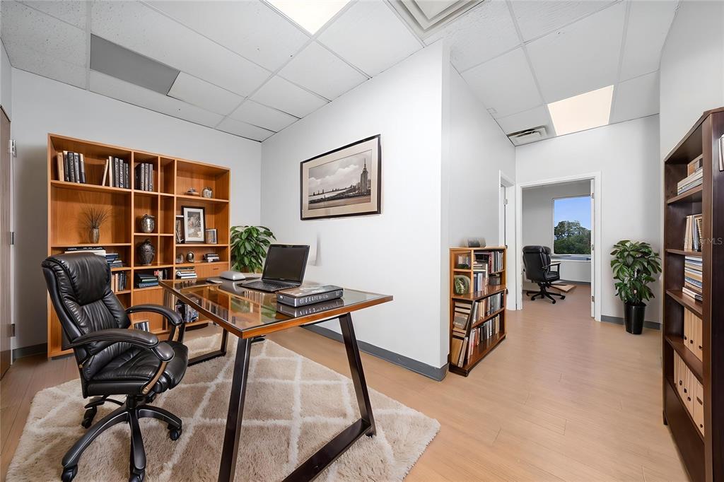 An office with a glass-top desk, black leather chair, bookshelves, and a view into another room — 7200 LAKE ELLENOR DRIVE UNIT 130, ORLANDO, FL
