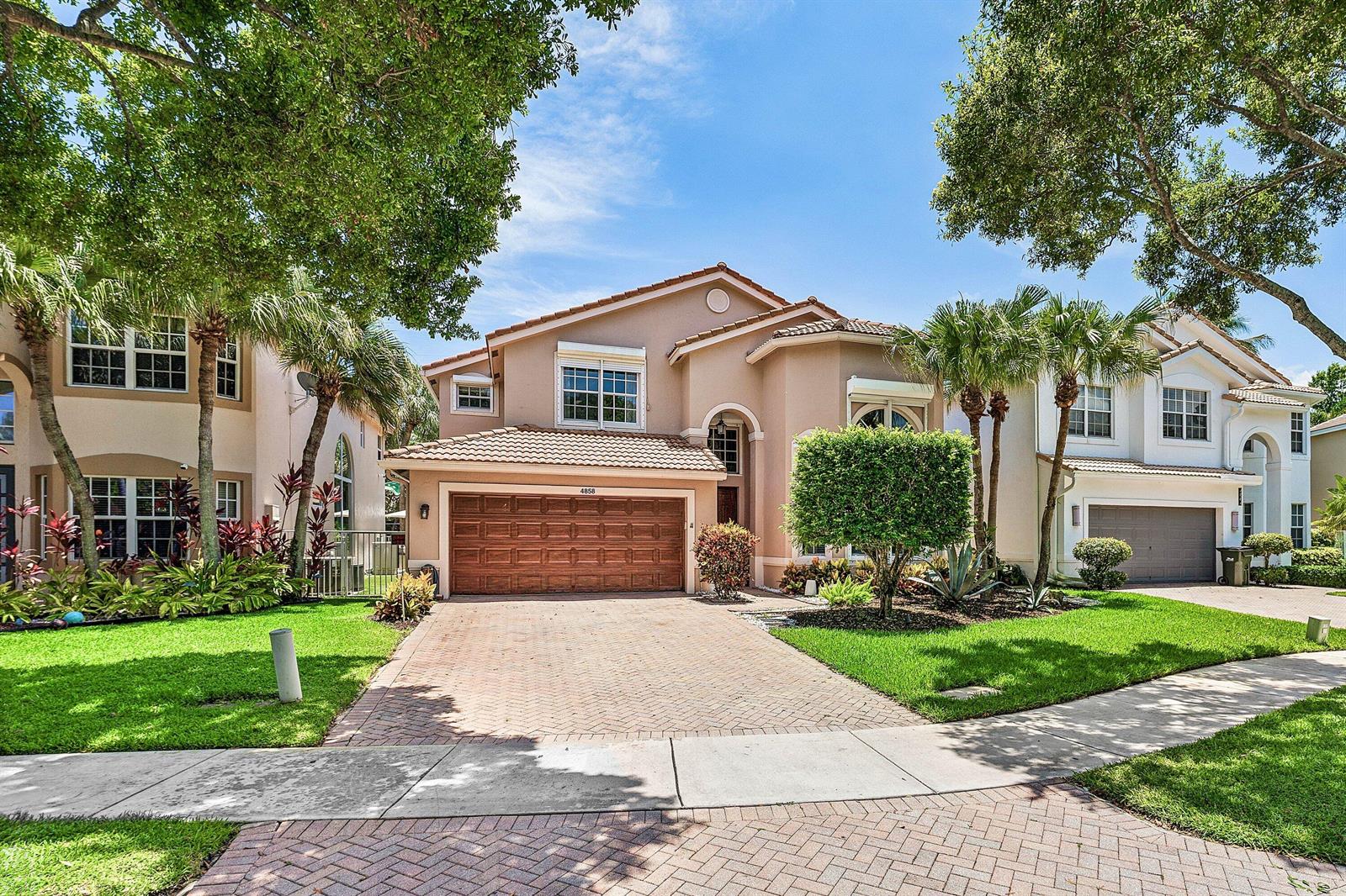 A two-story stucco house with a tiled roof and a brick driveway sits under trees — 4858 S Classical Boulevard, Delray Beach FL 33445, DELRAY BEACH, FL