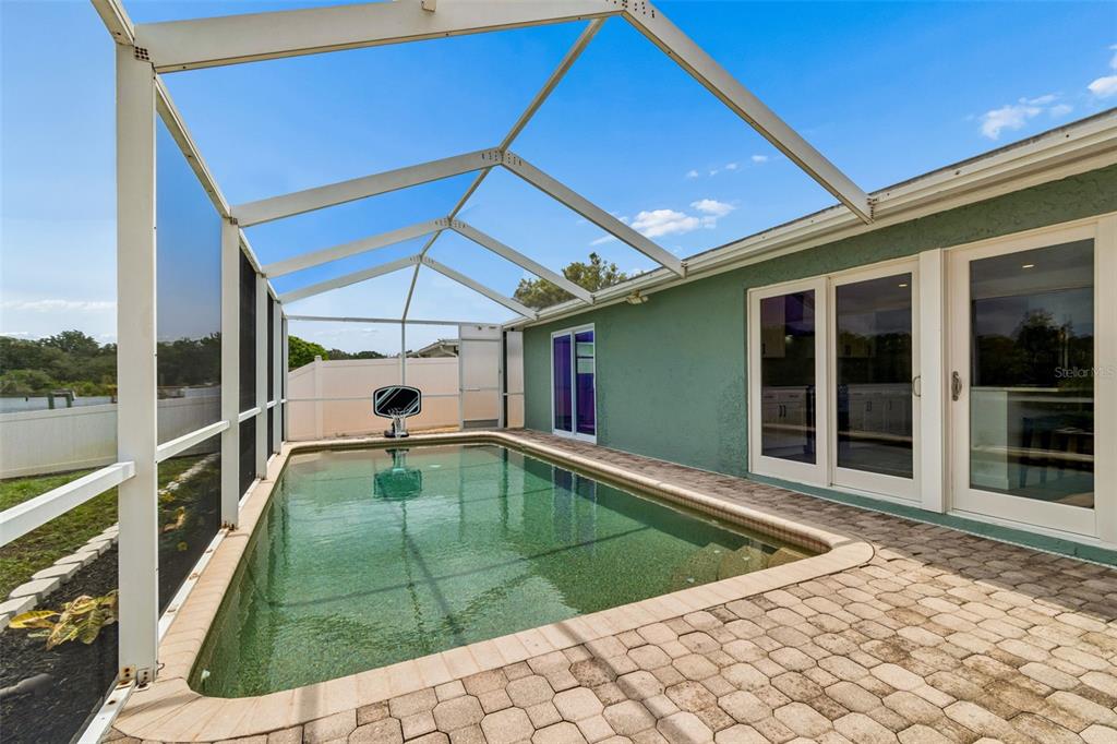 A swimming pool enclosed by a screened lanai with a paved deck and green exterior wall — 1166 CHANCELLOR DRIVE, HOLIDAY, FL