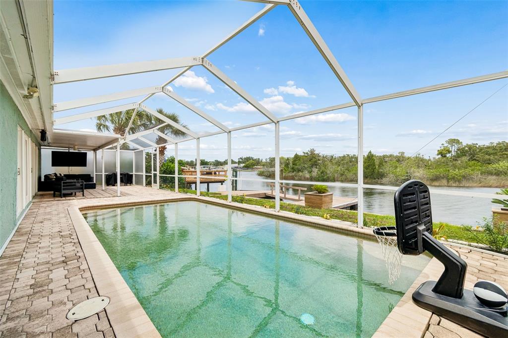 A screened-in pool patio overlooks a canal with a wooden dock and lush greenery — 1166 CHANCELLOR DRIVE, HOLIDAY, FL