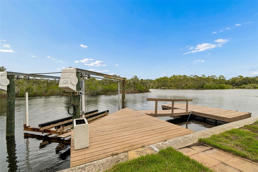 A wooden boat dock with a lift extends over a calm waterway under a blue sky — 1166 CHANCELLOR DRIVE, HOLIDAY, FL