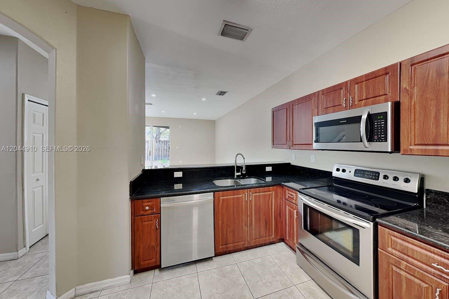 A kitchen features wood cabinets, stainless steel appliances, and black countertops — MIAMI, FL
