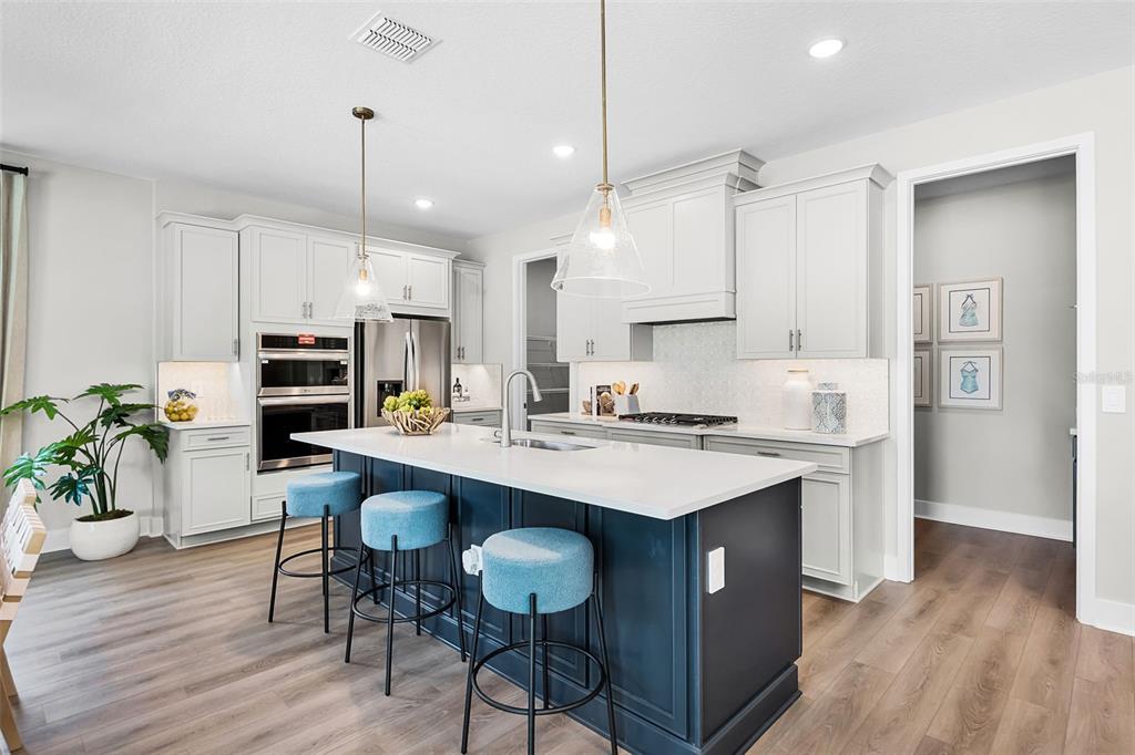 A modern kitchen features a dark blue island, white countertops, light gray cabinets, and stools — 714 EMERALD GROVE DRIVE, APOPKA, FL