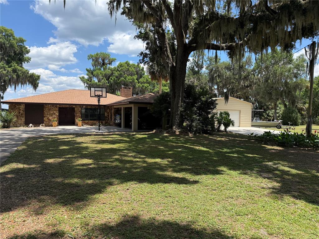 A single-story stone house with a large tree, a basketball hoop, and a detached garage — 4232 COUNTY ROAD 400, LAKE PANASOFFKEE, FL