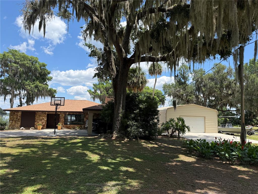 A single-story stone house with a detached metal garage and a large oak tree — 4232 COUNTY ROAD 400, LAKE PANASOFFKEE, FL
