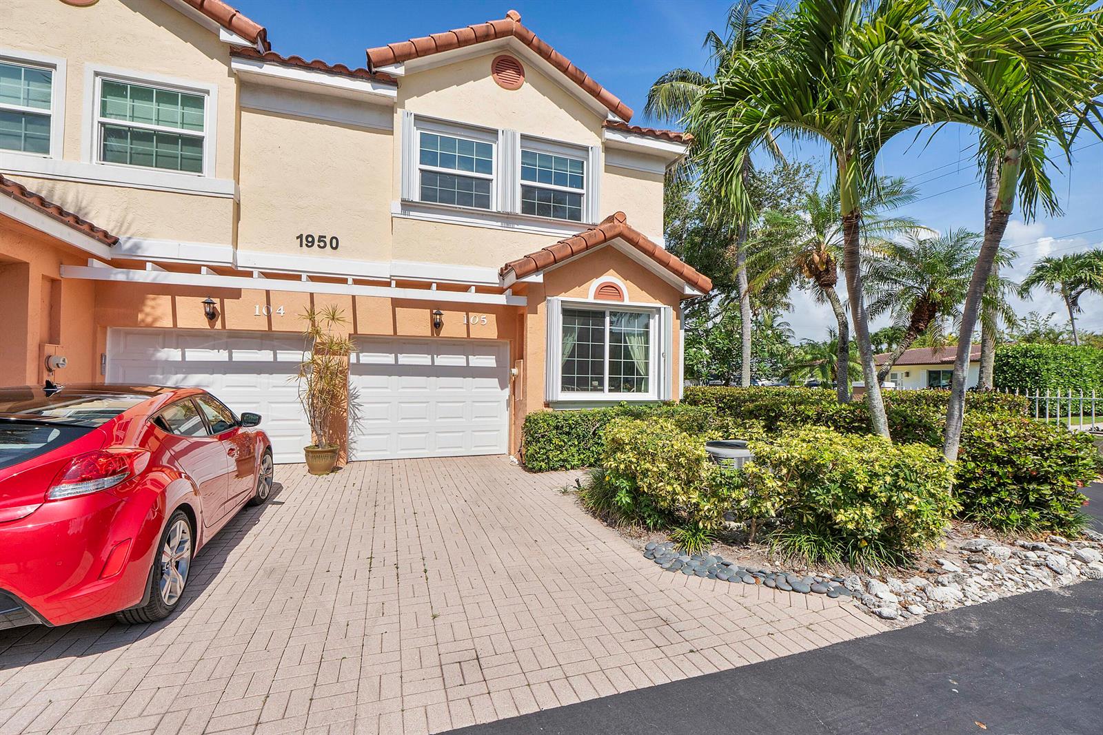 A two-story townhouse with a red car parked in the driveway and palm trees — 1950 Ne 7th St # 105, Deerfield Beach FL 33441, DEERFIELD BEACH, FL