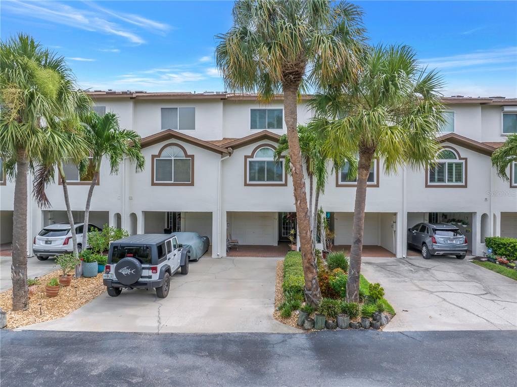 A row of multi-story townhomes with covered ground-level parking and palm trees in front — 117 YACHT CLUB LANE, TIERRA VERDE, FL