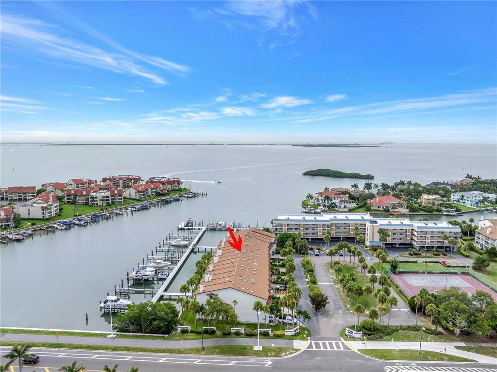 An aerial view shows a waterfront condominium complex with a boat dock and tennis courts — 117 YACHT CLUB LANE, TIERRA VERDE, FL
