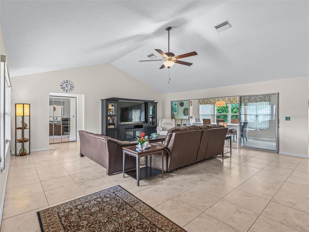 A living room with vaulted ceilings, tile flooring, a brown sectional sofa, and sliding glass doors — 11299 SE 175TH LANE, SUMMERFIELD, FL