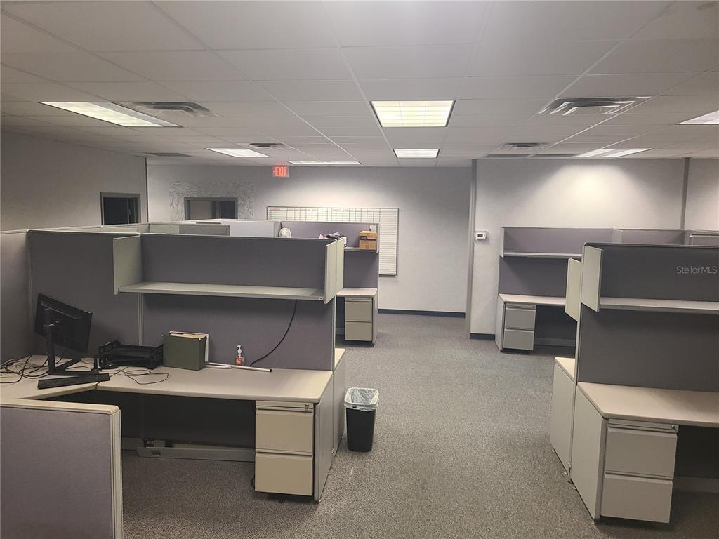 An office space features multiple gray cubicle workstations with desks and overhead storage shelves — 483 MONTGOMERY PLACE, ALTAMONTE SPRINGS, FL