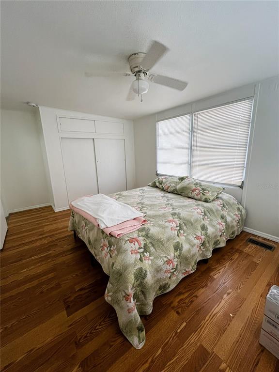 A bedroom features wood flooring, a ceiling fan, a floral bedspread, and white sliding closets — 6916 MARLIN LANE, BRADENTON, FL