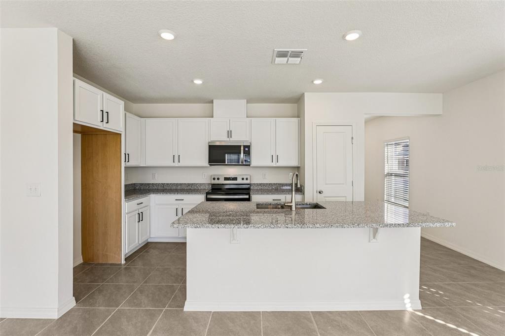 A kitchen features white cabinets, granite countertops, a center island, and stainless steel appliances — 387 SEQUOIA DRIVE, LAKE WALES, FL