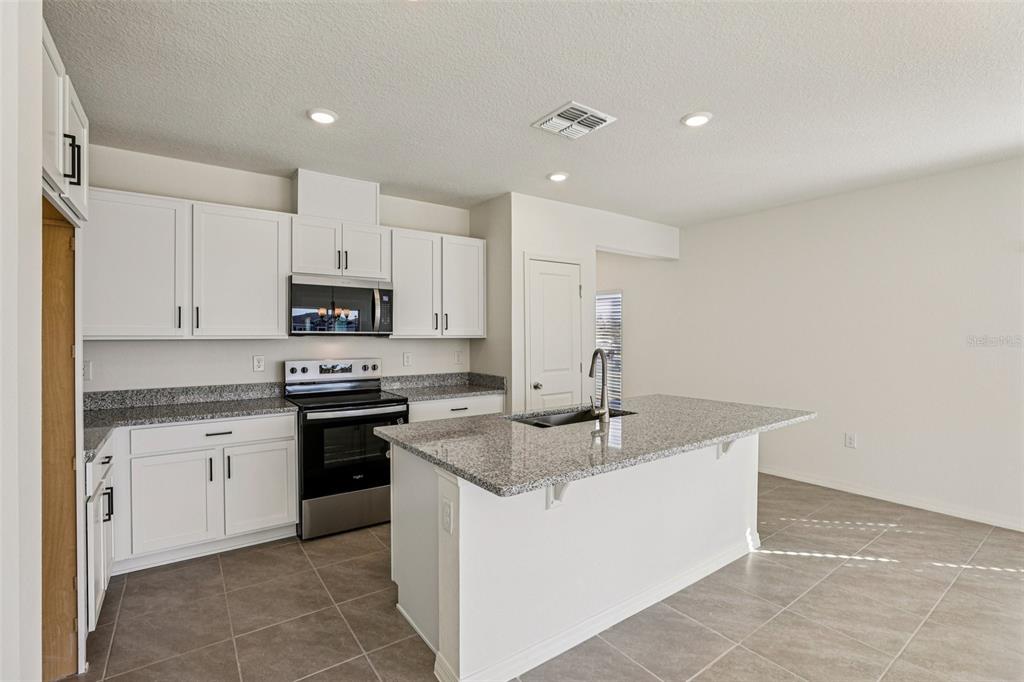 A kitchen features white cabinets, granite countertops, a center island, and stainless steel appliances — 387 SEQUOIA DRIVE, LAKE WALES, FL