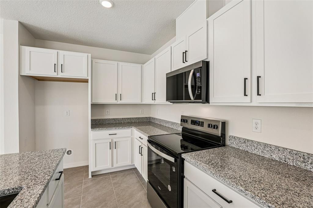 A kitchen features white cabinets, granite countertops, stainless steel appliances, and light-colored tile flooring — 387 SEQUOIA DRIVE, LAKE WALES, FL