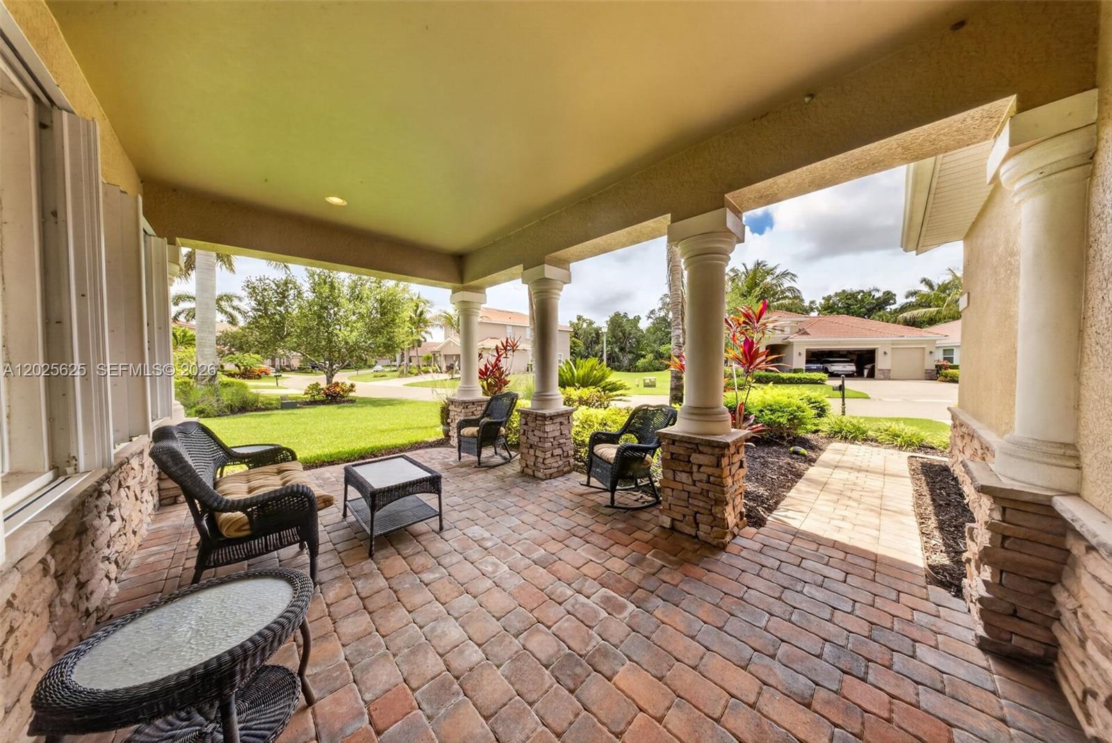 A covered brick patio features wicker furniture and stone-based columns overlooking a suburban lawn — NORTH FORT MYERS, FL