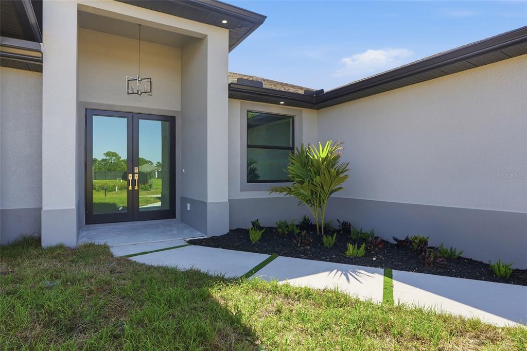 The exterior of a modern home features a double front door and a landscaped walkway — 431 PALMYRA AVENUE, LEHIGH ACRES, FL