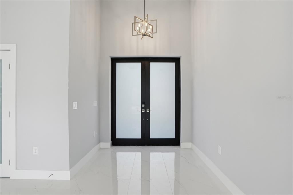 A bright entryway features white marble floors, light gray walls, and a modern geometric chandelier — 431 PALMYRA AVENUE, LEHIGH ACRES, FL