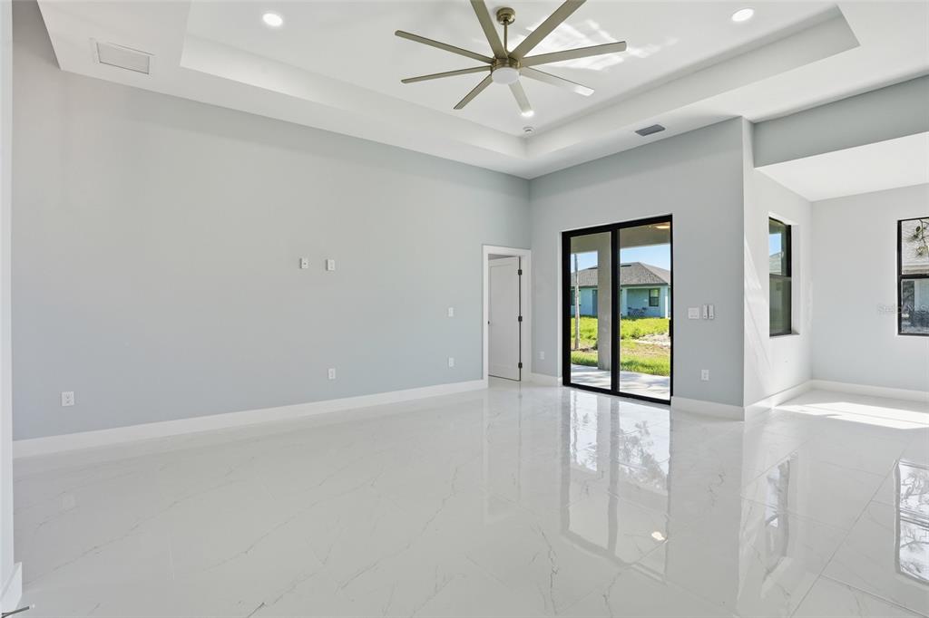 A bright living room features white marble-look tile floors, a tray ceiling, and sliding doors — 431 PALMYRA AVENUE, LEHIGH ACRES, FL