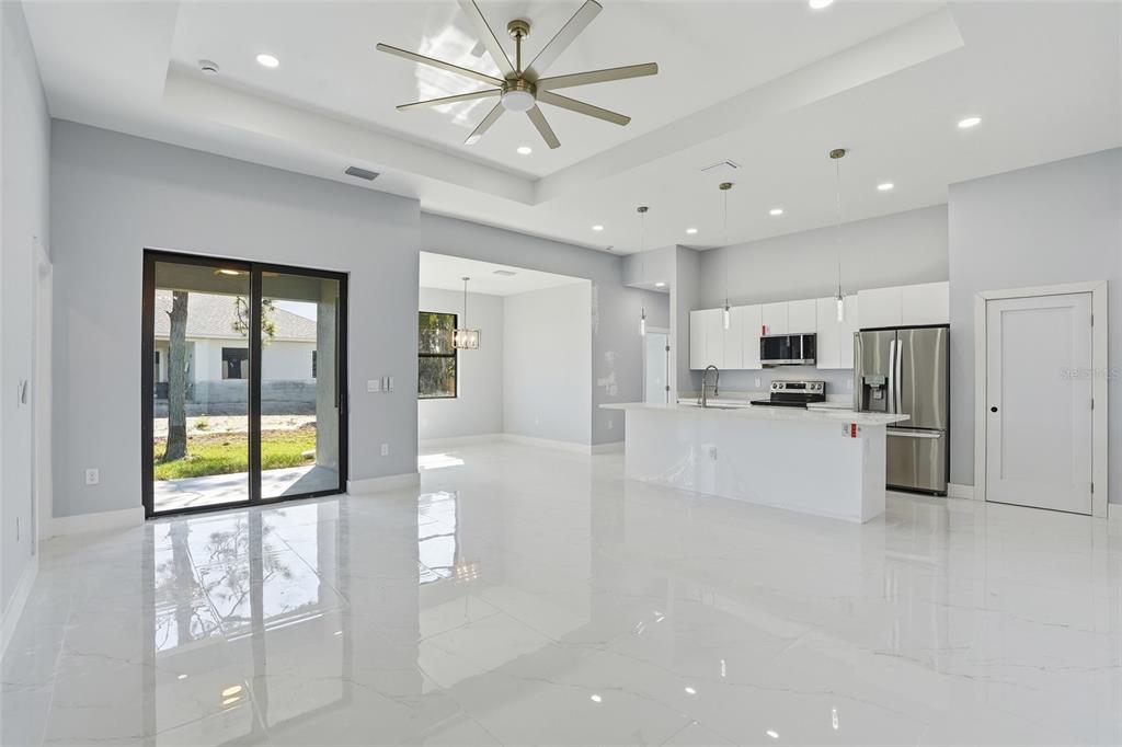 A bright, open-concept kitchen and living area features white cabinetry, stainless appliances, and tile flooring — 431 PALMYRA AVENUE, LEHIGH ACRES, FL