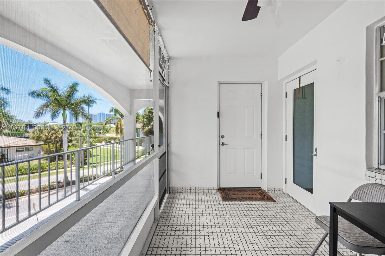 A screened-in balcony features white walls, tiled flooring, and views of palm trees outside — 541 Blue Heron Dr # 308, Hallandale Beach FL 33009, HALLANDALE BEACH, FL