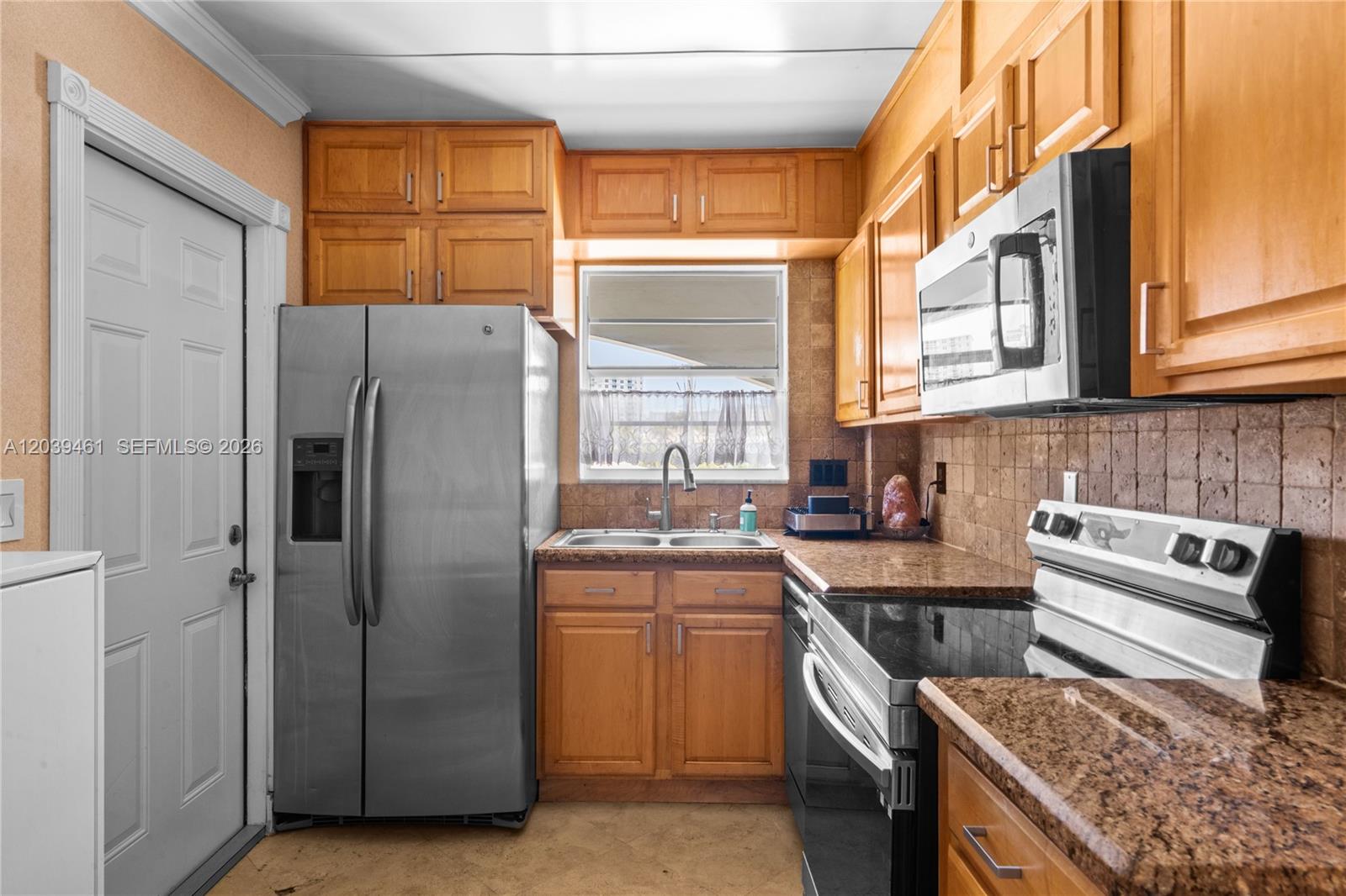 A kitchen features wood cabinets, granite countertops, stainless steel appliances, and a window above the sink — 541 Blue Heron Dr # 308, Hallandale Beach FL 33009, HALLANDALE BEACH, FL